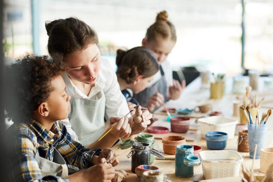 Young teacher showing one of pupils clay item and giving advice about painting it