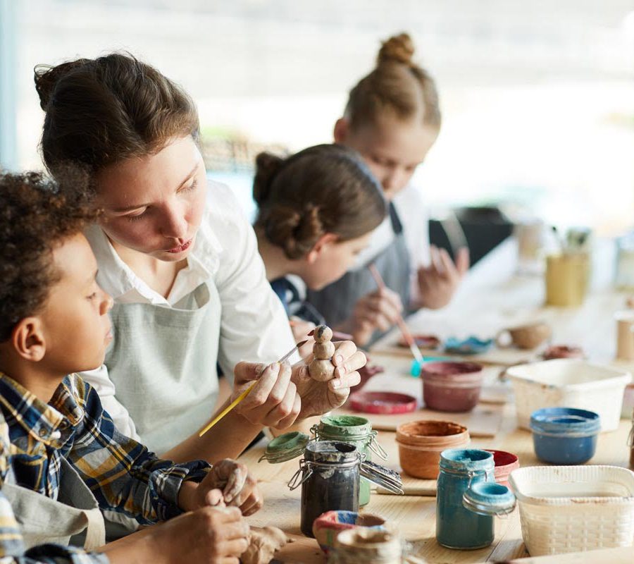 Young teacher showing one of pupils clay item and giving advice about painting it
