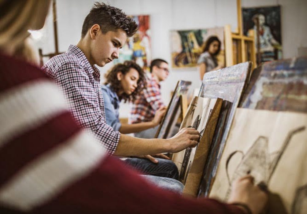 Group of students drawing their paintings on a class at art studio. Focus is on male student.