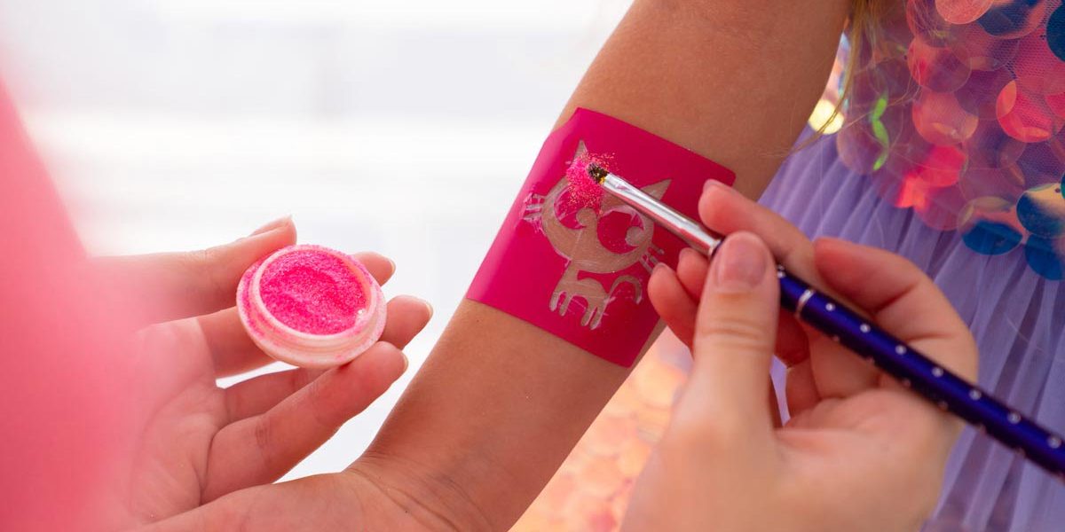the child makes a temporary tattoo of a kitten with pink sequins. decorative cosmetics for children and adults. shop.