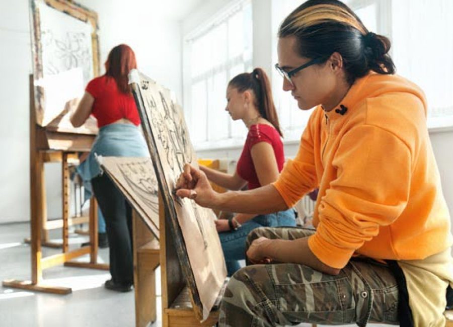 Closeup side view of group of high school students in an art class. They are drawing with charcoal pens. Each drawing is imaginary