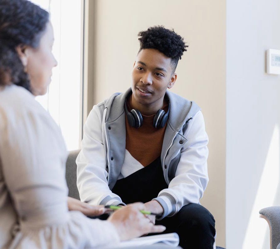 In therapy, the mid adult female counselor talks to the attentive young man and his unseen sister.