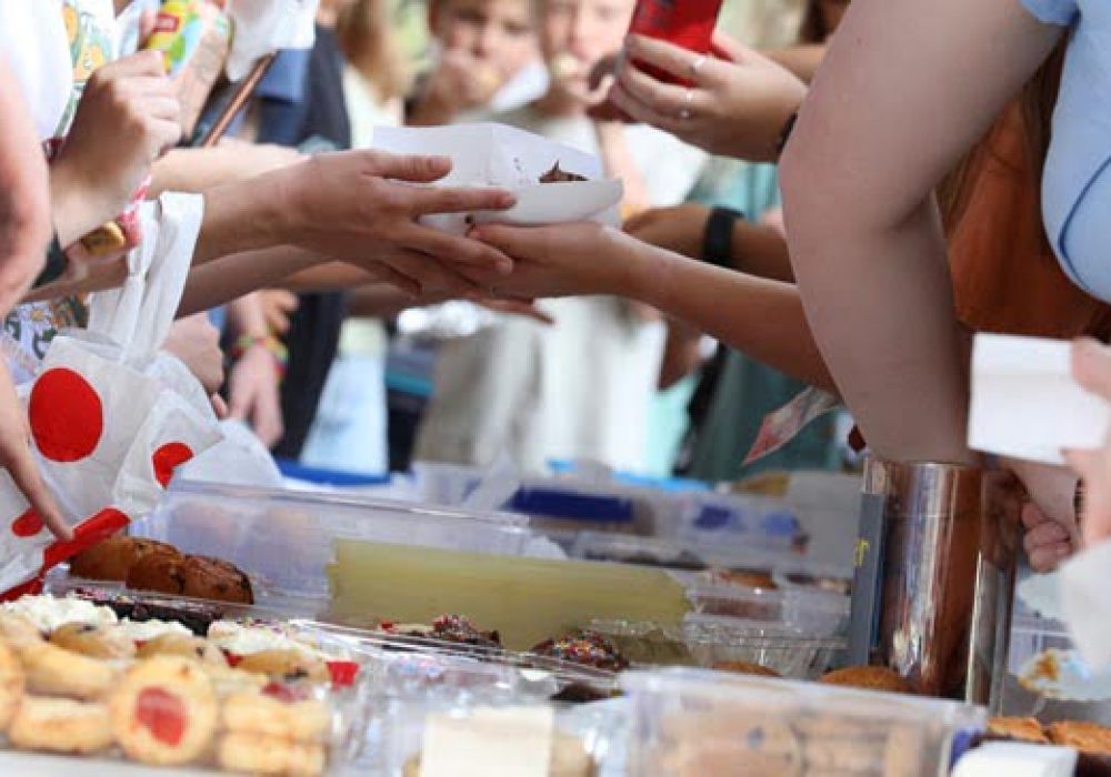 A close up of hands and food exchanging at a communty fair, fete or market stall. A typical bake or cake sale.