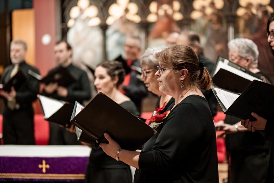 Church Choir during performance at Concert during Christmas Holiday season. Mixed age group of people dressed in all black attire. Interior of Anglican church at night.