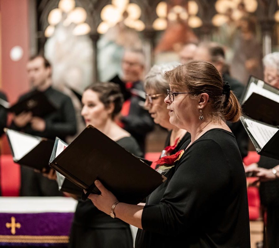 Church Choir during performance at Concert during Christmas Holiday season. Mixed age group of people dressed in all black attire. Interior of Anglican church at night.