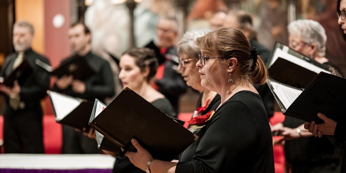 Church Choir during performance at Concert during Christmas Holiday season. Mixed age group of people dressed in all black attire. Interior of Anglican church at night.