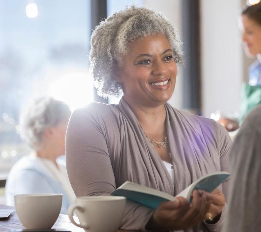 Smiling senior woman discusses a book with her unrecognizable husband while having coffee in local coffee shop.