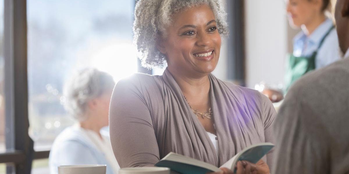 Smiling senior woman discusses a book with her unrecognizable husband while having coffee in local coffee shop.