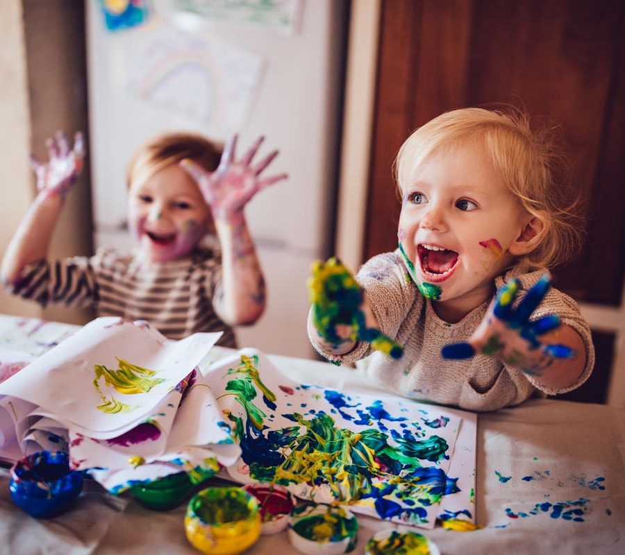 Happy little girls with dirty hands and faces having fun being creative with finger painting