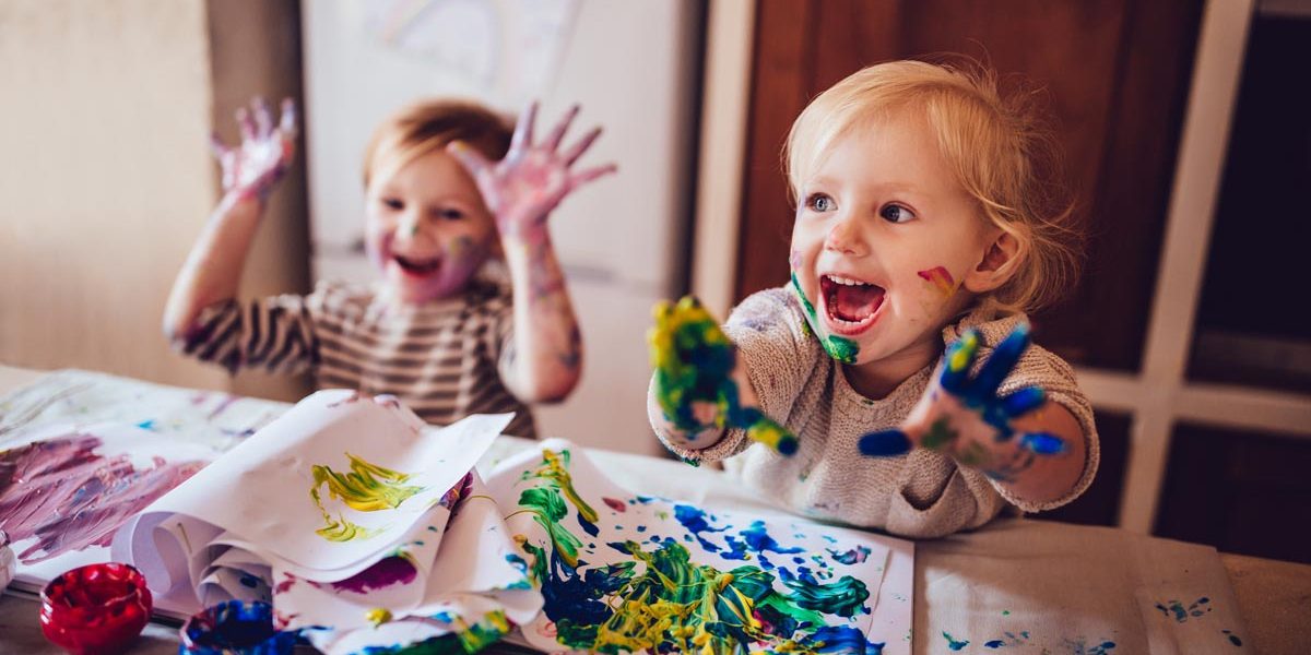 Happy little girls with dirty hands and faces having fun being creative with finger painting