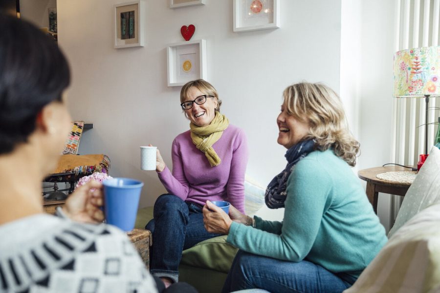 Mature women friends and sisters sitting together in a living room in Cornwall talking together.