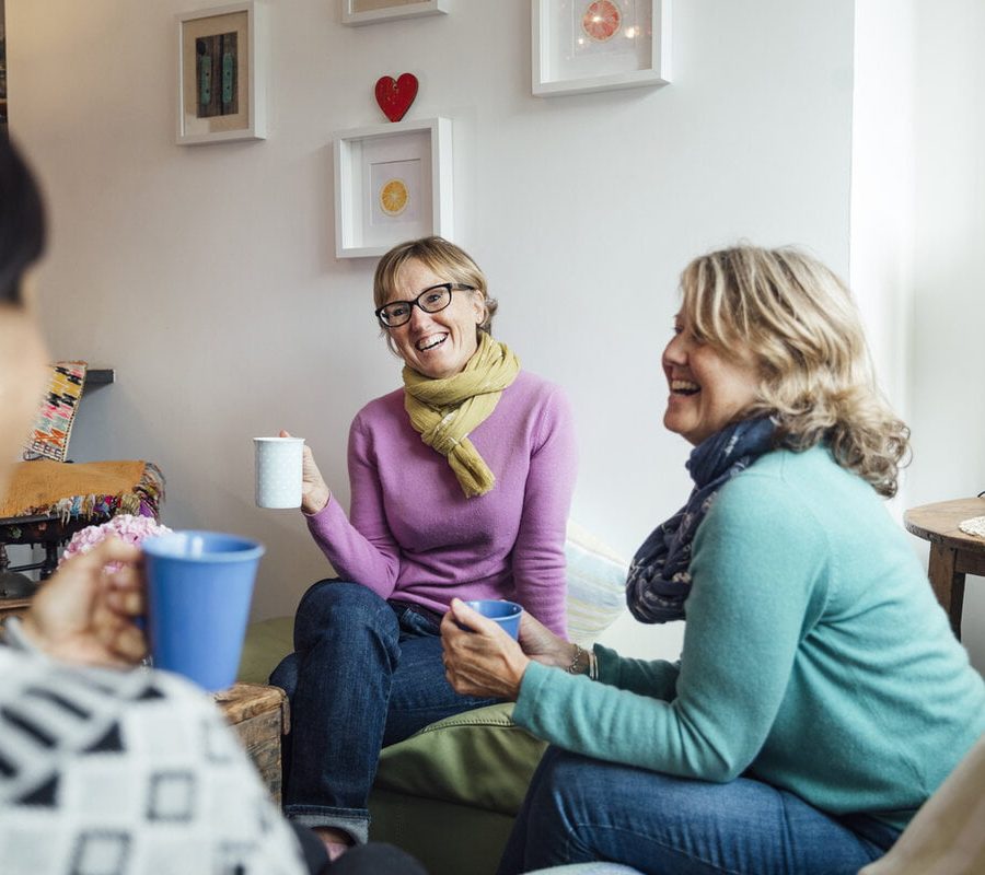 Mature women friends and sisters sitting together in a living room in Cornwall talking together.