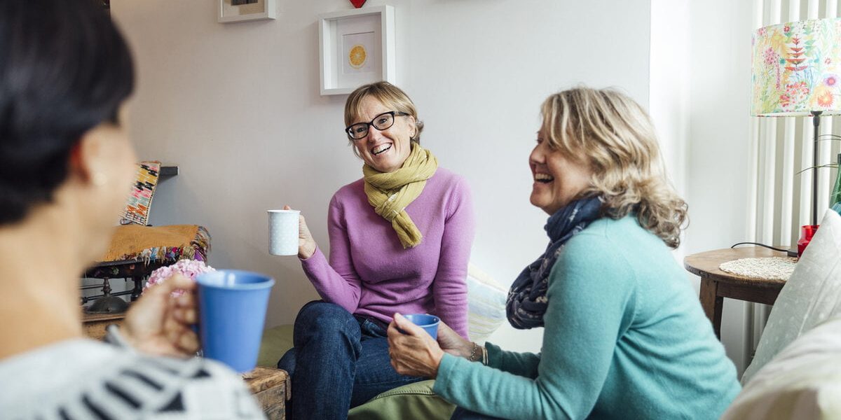 Mature women friends and sisters sitting together in a living room in Cornwall talking together.