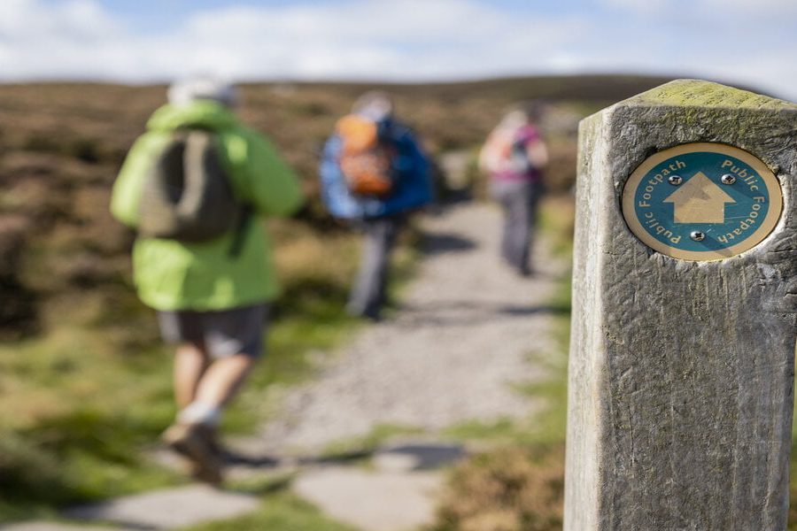 Out of focus shot tourists hiking uphill in Rothbury, Northumberland. The trail post is at the forefront of the shot and is the main focus.