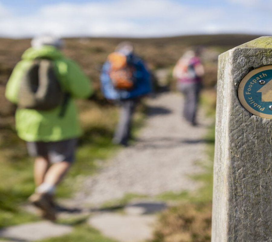 Out of focus shot tourists hiking uphill in Rothbury, Northumberland. The trail post is at the forefront of the shot and is the main focus.