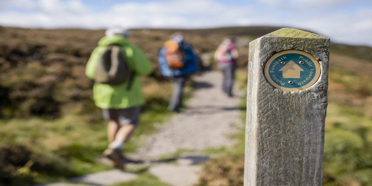 Out of focus shot tourists hiking uphill in Rothbury, Northumberland. The trail post is at the forefront of the shot and is the main focus.