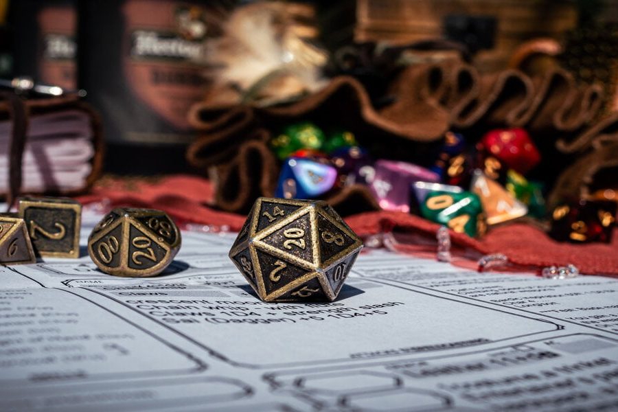 Low angle image of a brass 20-sided die on a character sheet in the sun. In the background are a dice bag and a notebook