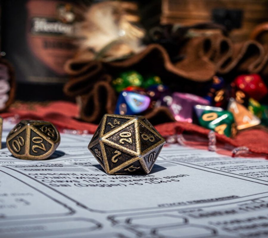 Low angle image of a brass 20-sided die on a character sheet in the sun. In the background are a dice bag and a notebook