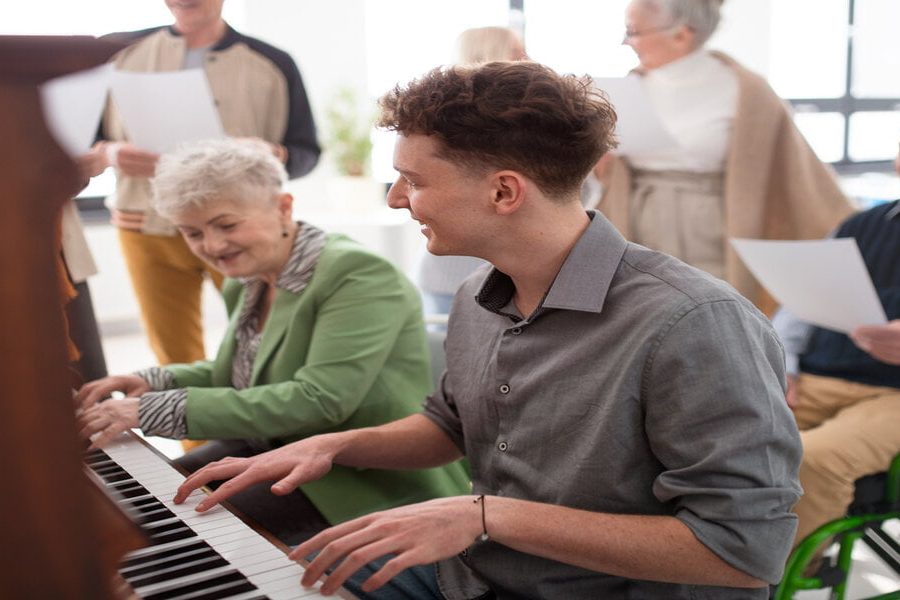A senior woman with young teacher playing at piano in choir rehearsal.