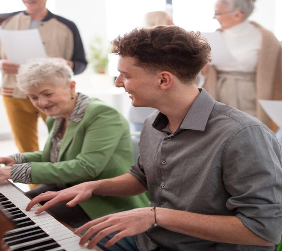 A senior woman with young teacher playing at piano in choir rehearsal.