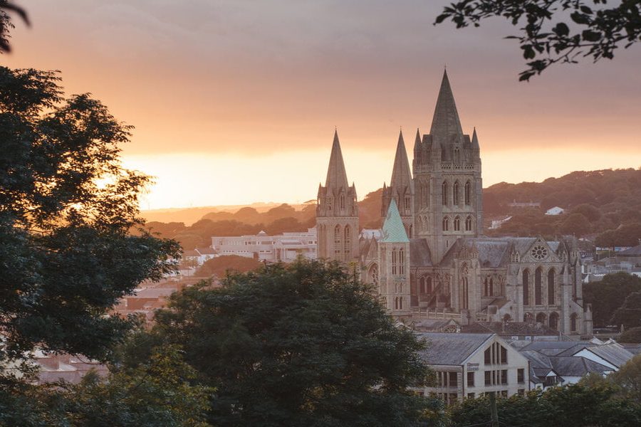 Beautiful warm sunlight illuminates Truro Cathedral in Cornwall's capital city as the sun sets. Trees form a frame around the image.