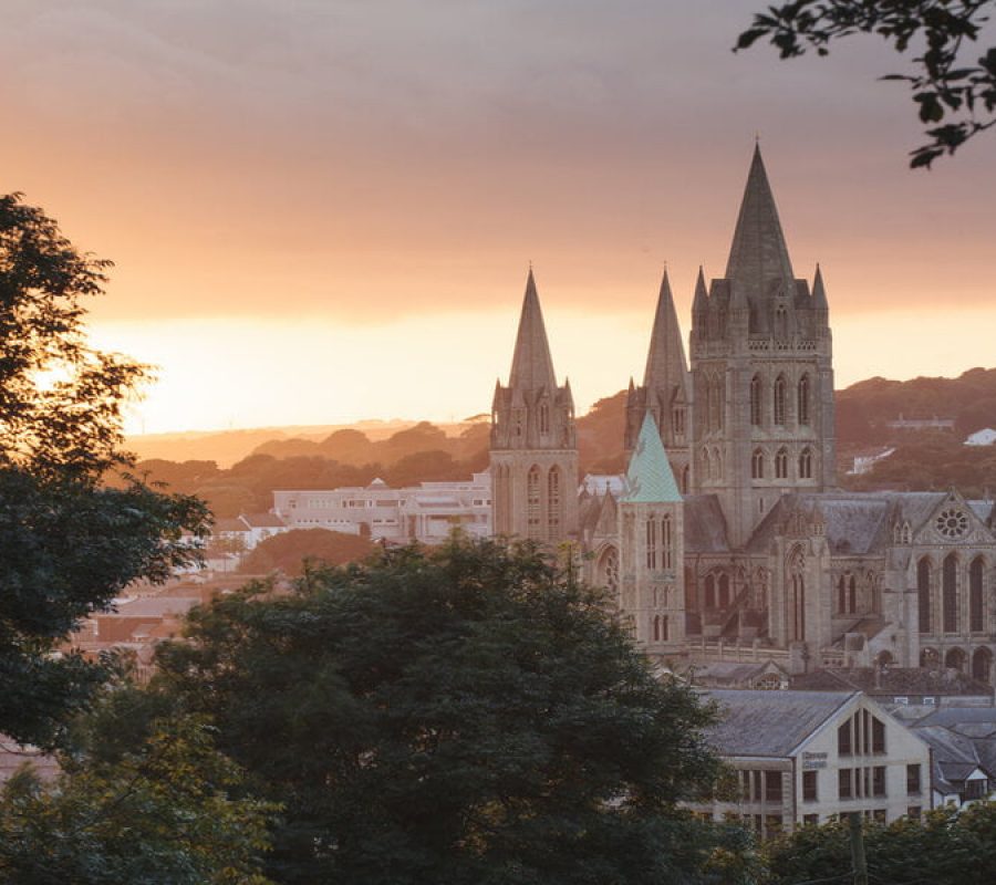 Beautiful warm sunlight illuminates Truro Cathedral in Cornwall's capital city as the sun sets. Trees form a frame around the image.