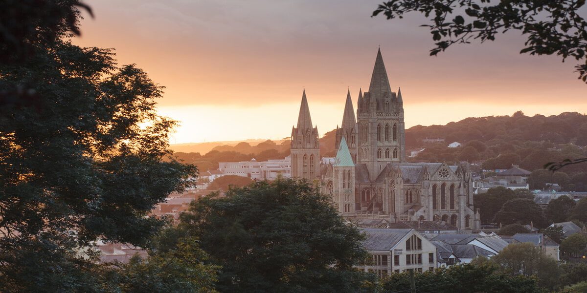 Beautiful warm sunlight illuminates Truro Cathedral in Cornwall's capital city as the sun sets. Trees form a frame around the image.