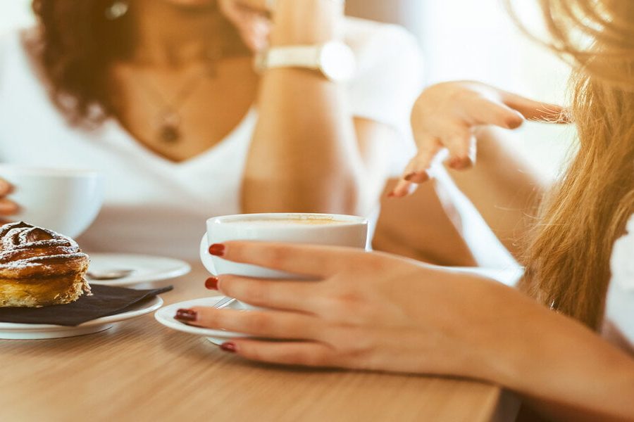 Two young and beautiful women meet at the bar for a cappuccino and to chat. A woman speaks gesturing while the other is listening