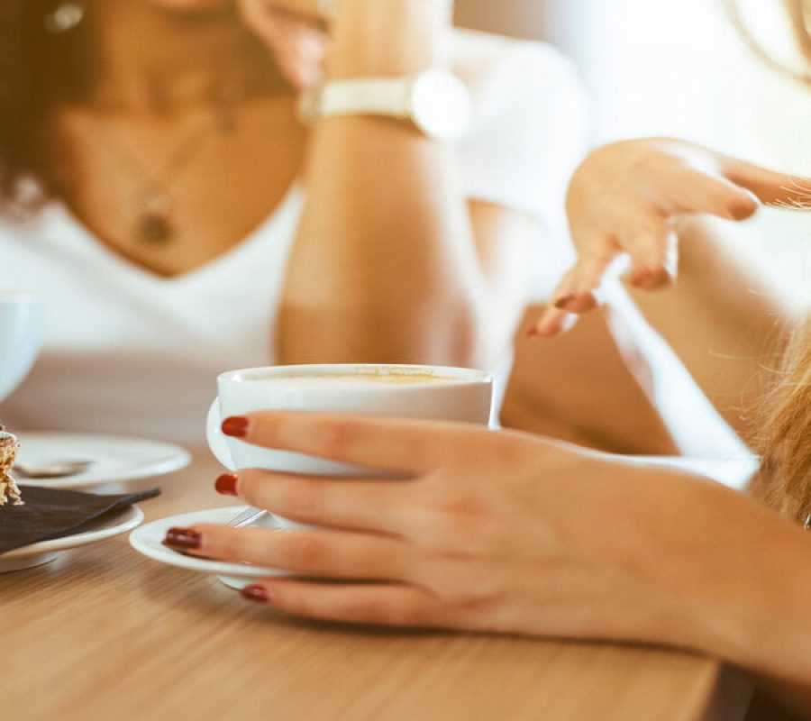Two young and beautiful women meet at the bar for a cappuccino and to chat. A woman speaks gesturing while the other is listening