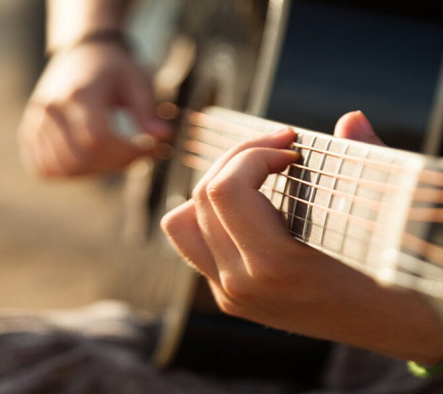 Teen girl playing acoustic guitar, detail, shallow DOF.