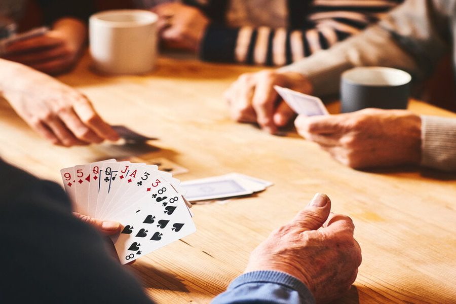 Close up of senor man's hand playing cards with friends at care home