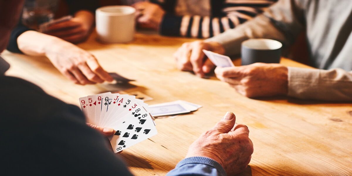 Close up of senor man's hand playing cards with friends at care home